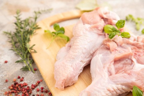 Raw turkey wing with herbs and spices on a wooden cutting board on a brown concrete background.