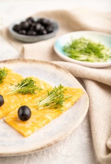 Marble cheese with olives and watercress microgreen on gray concrete background and linen textile.