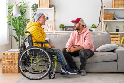 Disabled man in wheelchair and friends chatting relaxed in the living room of the house