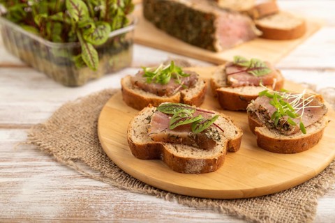 Bread sandwiches with jerky salted meat, sorrel and cilantro microgreen on white wooden background