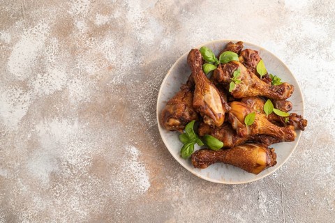 Smoked chicken legs with herbs and spices on a ceramic plate on a brown concrete background. Top