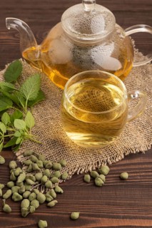 Green oolong tea with herbs in glass on brown wooden background and linen textile. Healthy drink