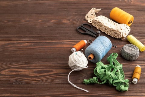 Sewing accessories: scissors, thread, thimbles, braid on brown wooden background. Side view, copy
