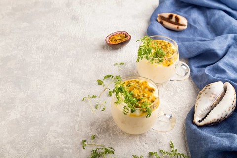Yogurt with passionfruit and marigold microgreen in glass on gray concrete background with blue