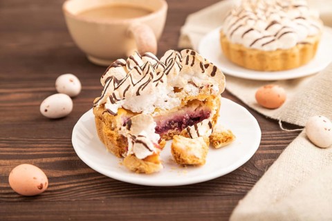 Tartlets with meringue cream and cup of coffee on brown wooden background and linen textile. side