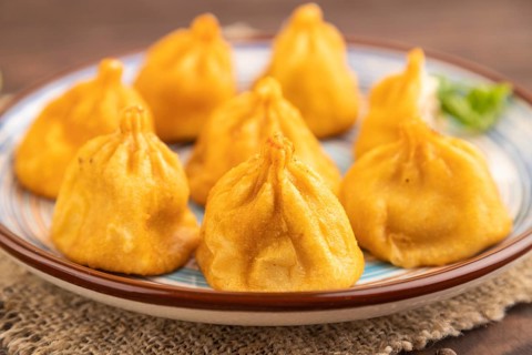 Fried manti dumplings with pepper, basil on brown wooden background and linen textile. Side view,