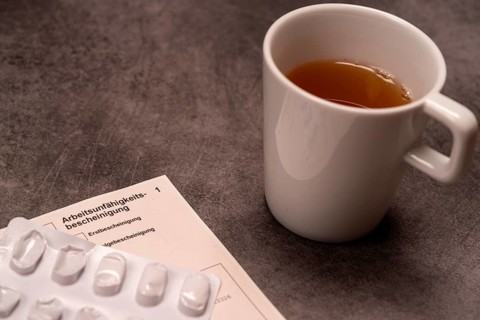A cup of tea next to medication and a certificate of incapacity for work on a grey background