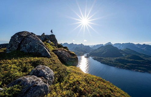 Mountaineer on the summit of Dronningsvarden or Stortinden, behind sea and fjord Umvagsundet,