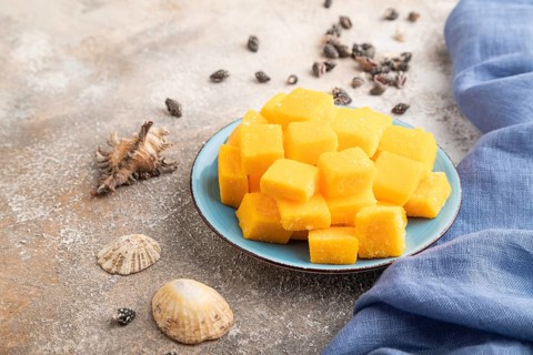 Dried and candied mango cubes on blue plate on brown concrete background and linen textile. Side