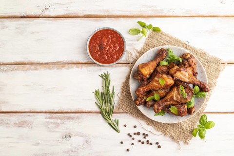 Smoked chicken legs with herbs and spices on a ceramic plate with linen textile on a white wooden
