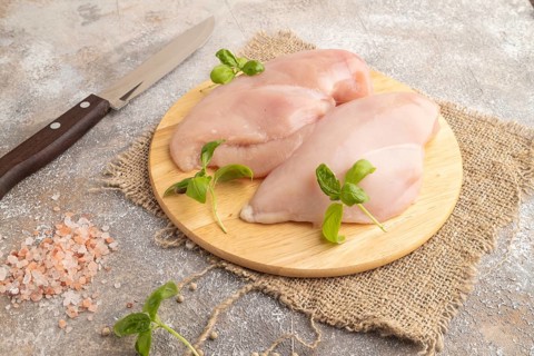 Raw chicken breast with herbs and spices on a wooden cutting board on a brown concrete background.