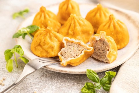 Fried manti dumplings with pepper, basil on gray concrete background and linen textile. Side view,