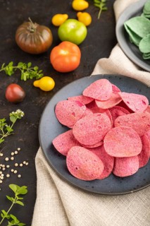 Green and red potato chips with herbs and tomatoes on black concrete background and linen textile.