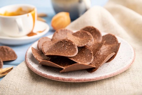 Chocolate chips with cup of coffee and caramel on a blue wooden background and linen textile. side