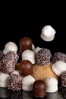 Pile of different chocolate kisses on a dark background, coconut half, one flying