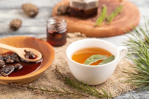 Pine cone jam with herbal tea on gray wooden background and linen textile. Side view, close up,