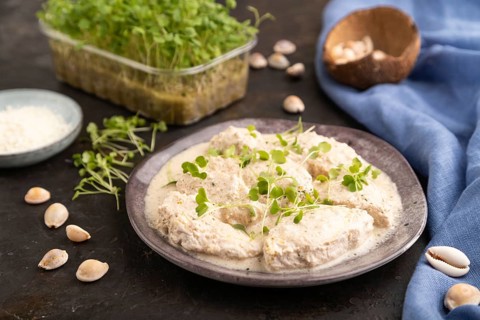 Stewed chicken fillets with coconut milk sauce and rucola microgreen on black concrete background