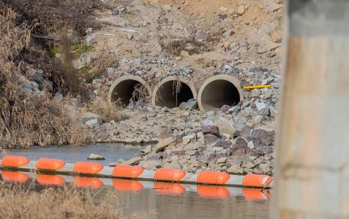 Three water drainage culverts in side of hill that empty into shallow river. Bridge support column