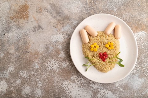 Funny mixed quinoa porridge, sweet corn, pomegranate seeds and small sausages in form of cat face