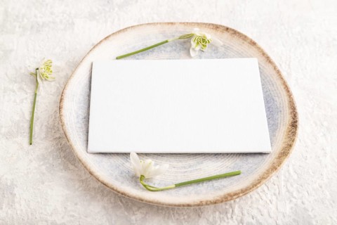 White paper invitation card, mockup with galanthus snowdrop flowers on ceramic plate and gray