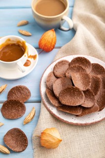 Chocolate chips with cup of coffee and caramel on a blue wooden background and linen textile. side