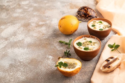 Yoghurt with granadilla and mint in clay bowl on brown concrete background and orange linen textile