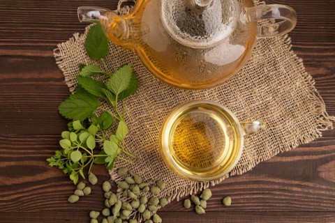 Green oolong tea with herbs in glass on brown wooden background and linen textile. Healthy drink