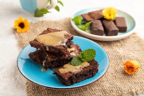 Chocolate brownie with caramel sauce with a cup of coffee on gray concrete background and linen