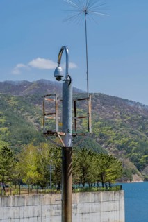 Round closed circuit camera on curved pole with lake and mountain under blue sky in background