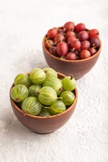 Fresh red and green gooseberry in clay bowl on gray concrete background. side view, close up