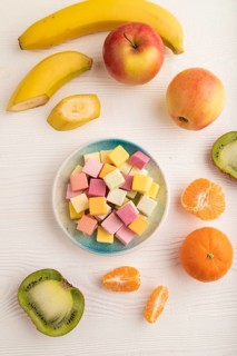 Various fruit jelly chewing candies on plate on white wooden background. apple, banana, tangerine,