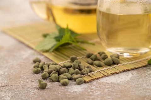 Green oolong tea with herbs in glass on brown concrete background. Healthy drink concept. Side