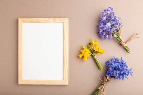 Wooden frame with spring snowdrop flowers bluebells, narcissus on beige pastel background. top