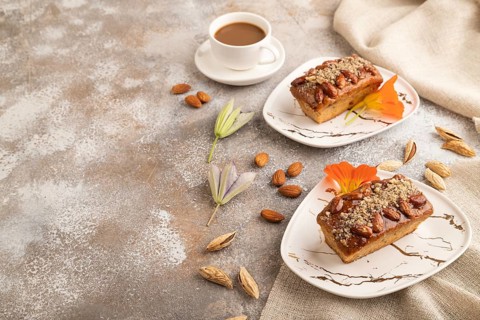 Caramel and almond cake with cup of coffee on brown concrete background and linen textile. side