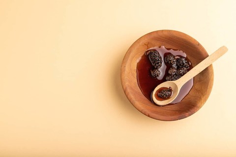 Pine cone jam in wooden bowl on orange pastel background. Top view, flat lay, copy space