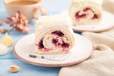 Roll biscuit cake with cream cheese and jam, cup of coffee on blue wooden background and linen