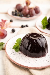 Black currant and grapes jelly on white wooden background and linen textile. side view, close up,