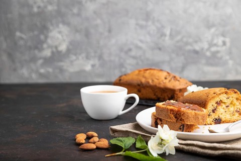 Homemade cake with raisins, almonds, soft caramel and a cup of coffee on a black concrete