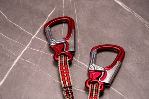Two red carabiners with safety ropes on a grey stone-like background, studio photo, Germany, Europe