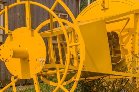 Bottom steel framework of ocean buoy laying in grass next to old rusty storage building in fishing