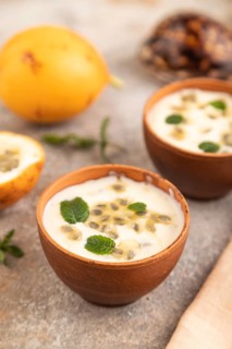Yoghurt with granadilla and mint in clay bowl on brown concrete background and orange linen textile