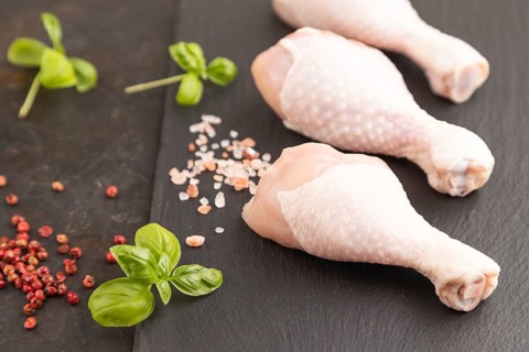 Raw chicken legs with herbs and spices on a black slate cutting board on a black concrete