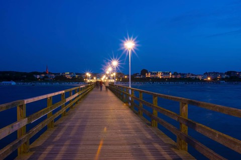 Nocturnal pier with illuminated street lamps and star effect, illuminated pier with strolling