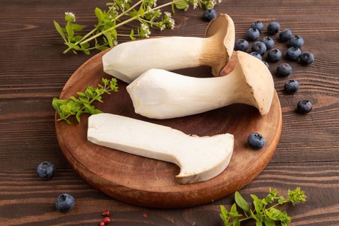 King Oyster mushrooms or Eringi (Pleurotus eryngii) on brown wooden background with blueberry,
