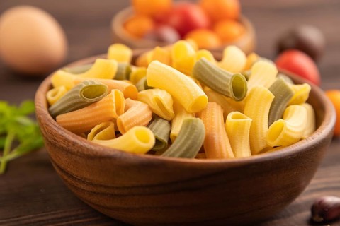 Rigatoni colored raw pasta with tomato, eggs, spices, herbs on brown wooden background. Side view,