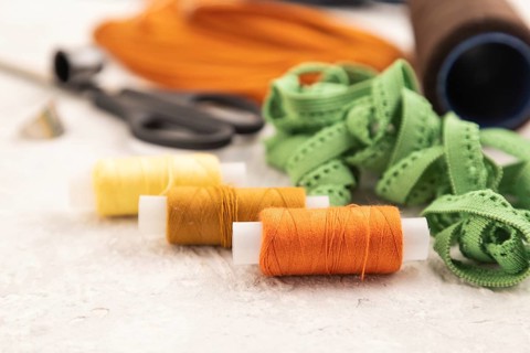 Sewing accessories: scissors, thread, thimbles, braid on gray concrete background. Side view, close
