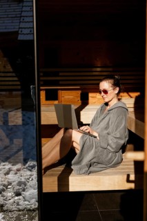 Woman sits with laptop in the sauna