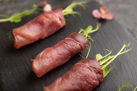 Slices of smoked salted meat with green pea microgreen on black concrete background. Side view,