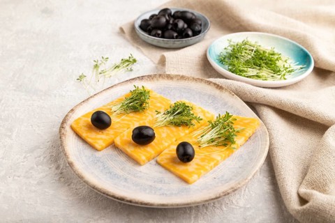 Marble cheese with olives and watercress microgreen on gray concrete background and linen textile.