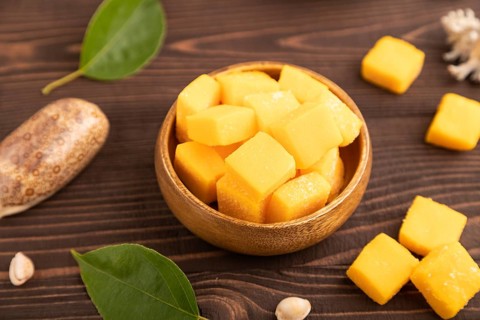 Dried and candied mango cubes in wooden bowls on brown wooden textured background. Side view, close